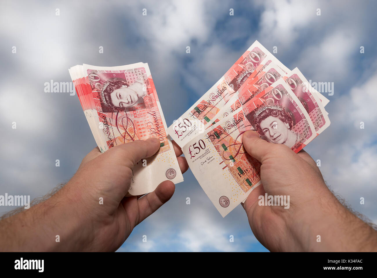 Pair of hands counting new style GBP £50 notes sterling with blue sky and cloud background. Stock Photo