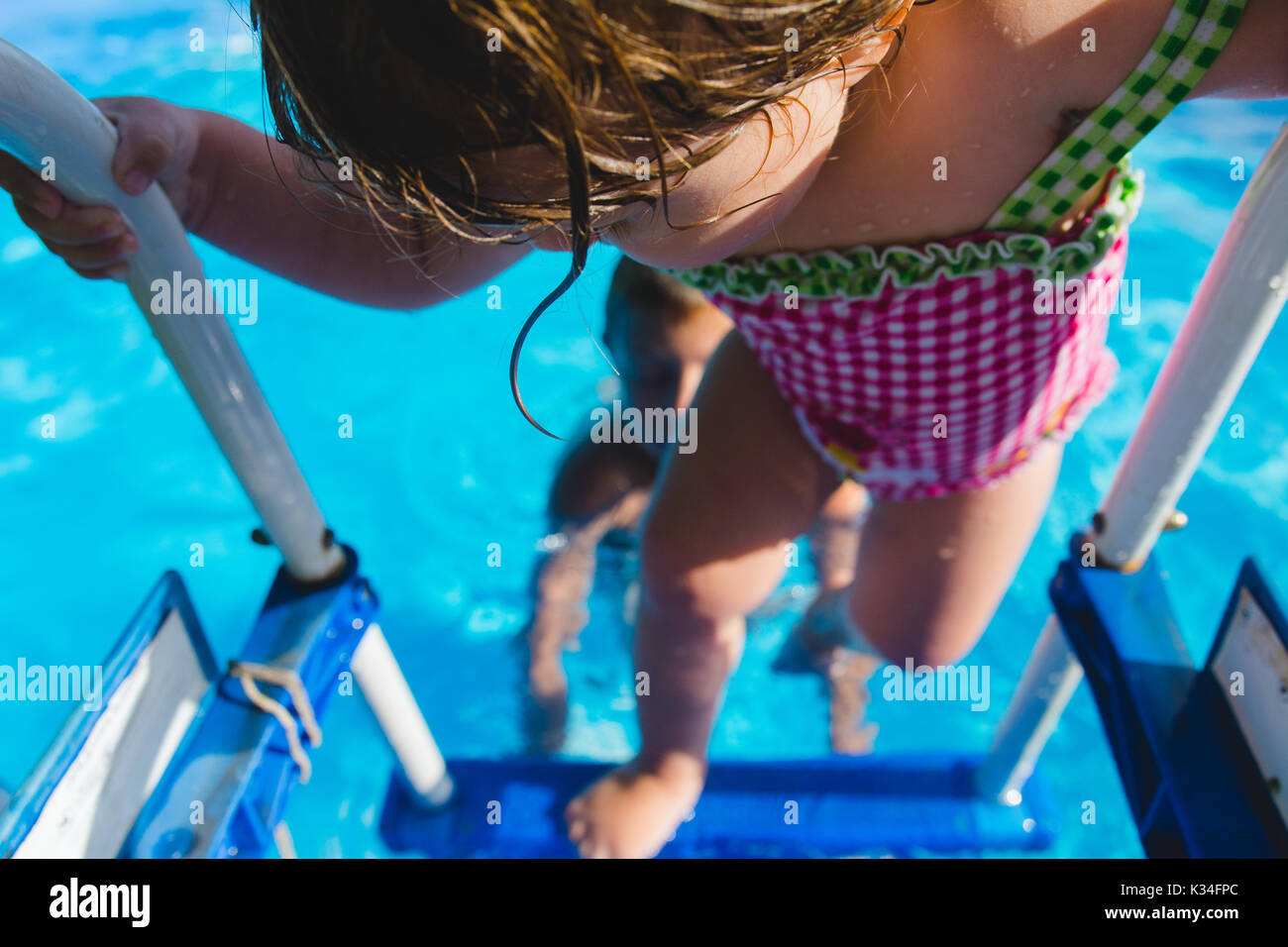 A young girl climbs out of a swimming pool during  the summer. Stock Photo