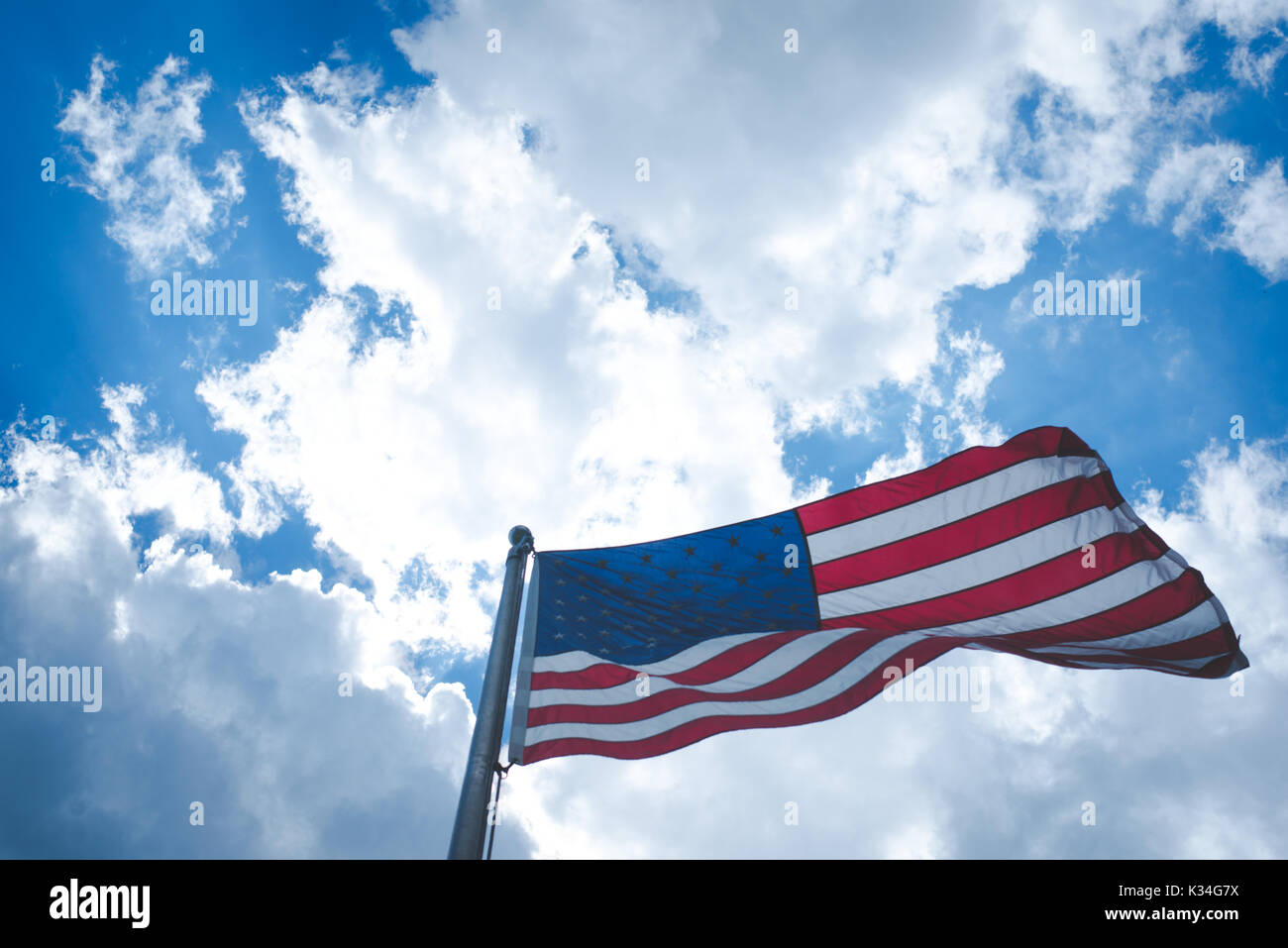 An American flag blows in the wind against a blue sky with clouds. Stock Photo