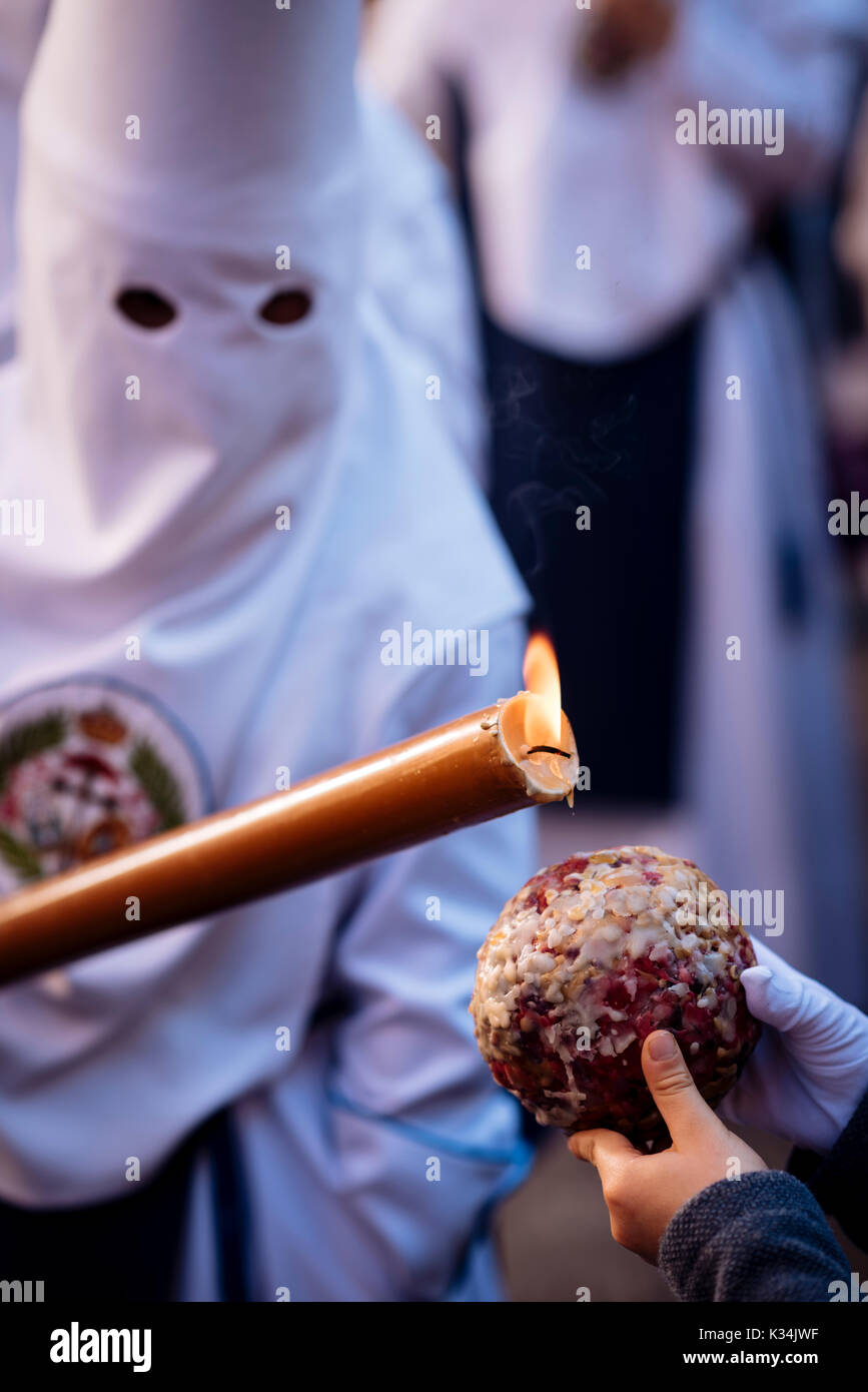 A Penitent of 'Los Negritos' Brotherhood dripping candle wax onto a boy's wax ball during Semana Santa (Holy Week), Seville, Andalucia, Spain Stock Photo