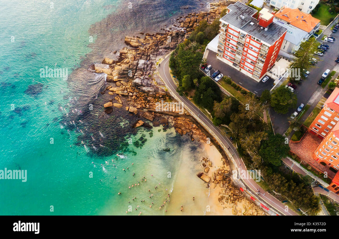 Overhead view of crowd of swimmers going for a regular race swim at Manly beach in Sydney, Australia, around coastal cliff and residential houses. Stock Photo