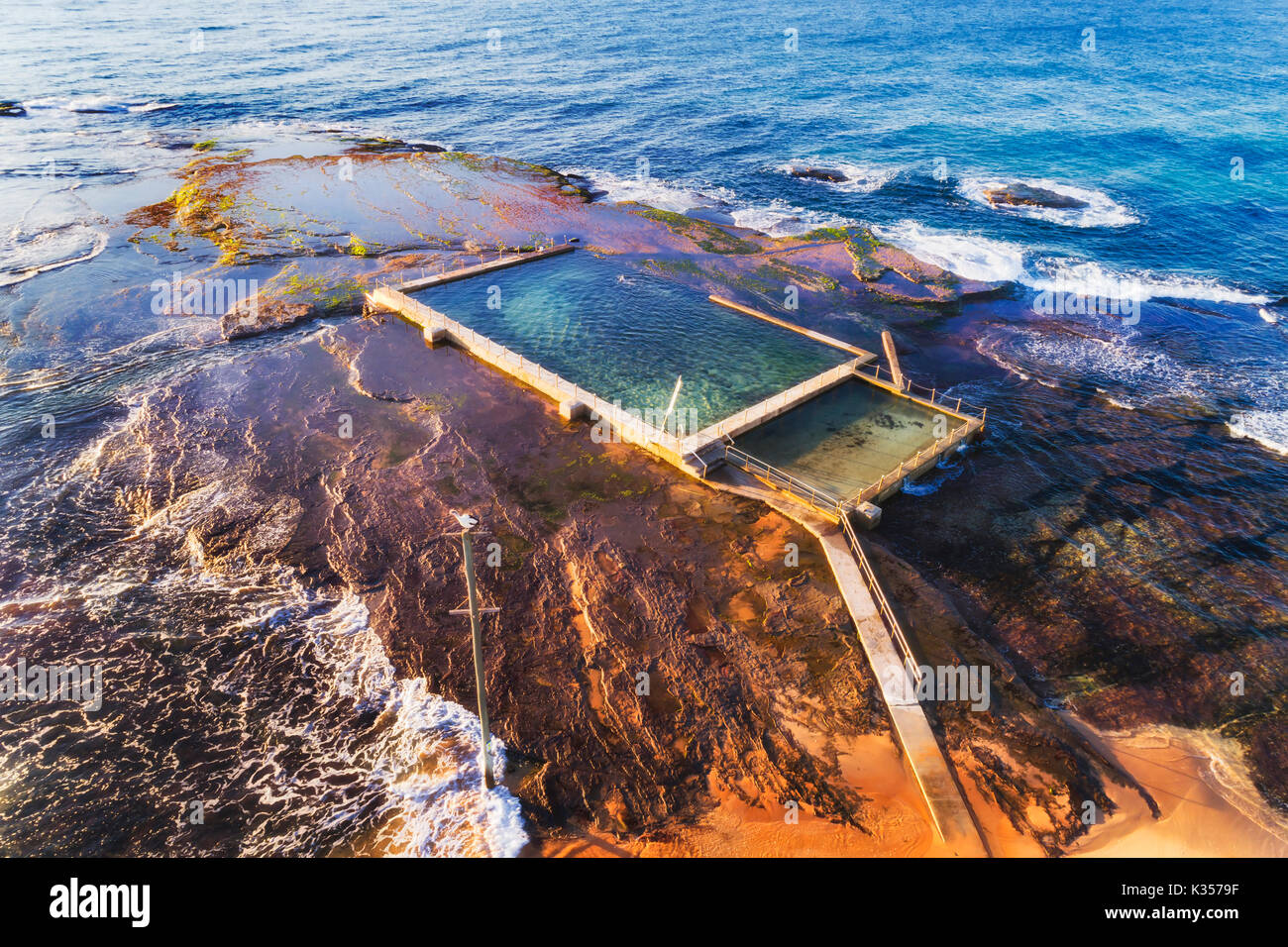 Remote isolated rock pool off Mona Vale beach at high tide with swimmer breaking waves of Pacific ocean coast in Sydney. Stock Photo