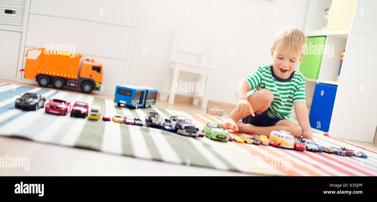 Little child playing with toy cars. Boy sitting on the floor at home ...