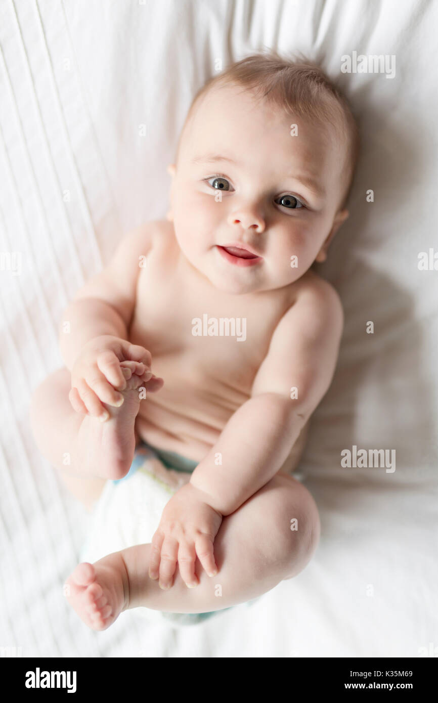 Cute happy 7 month baby girl in diaper lying and playing Stock Photo