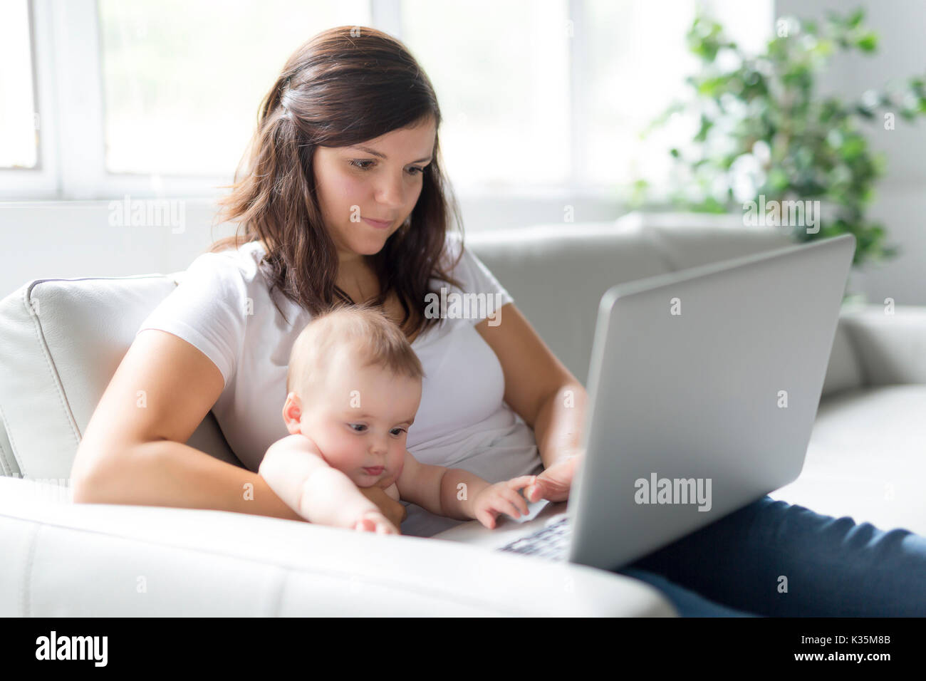 mother and baby child are looking to play and read computer on the couch at home Stock Photo