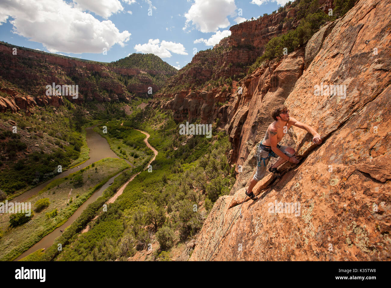 A young, male rock climber leading a route in a red rock canyon in the ...