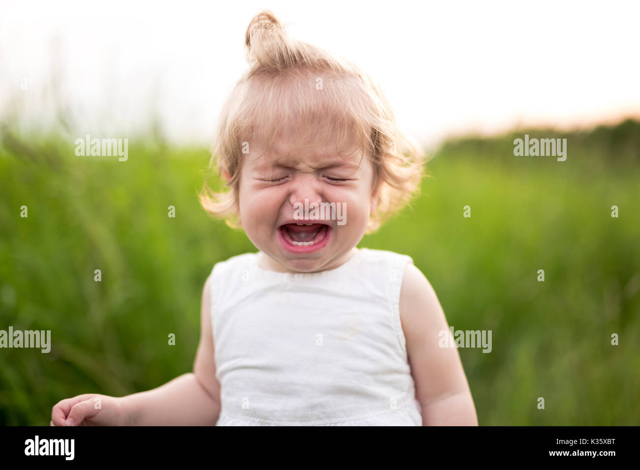 Crying baby alone in the meadow Stock Photo