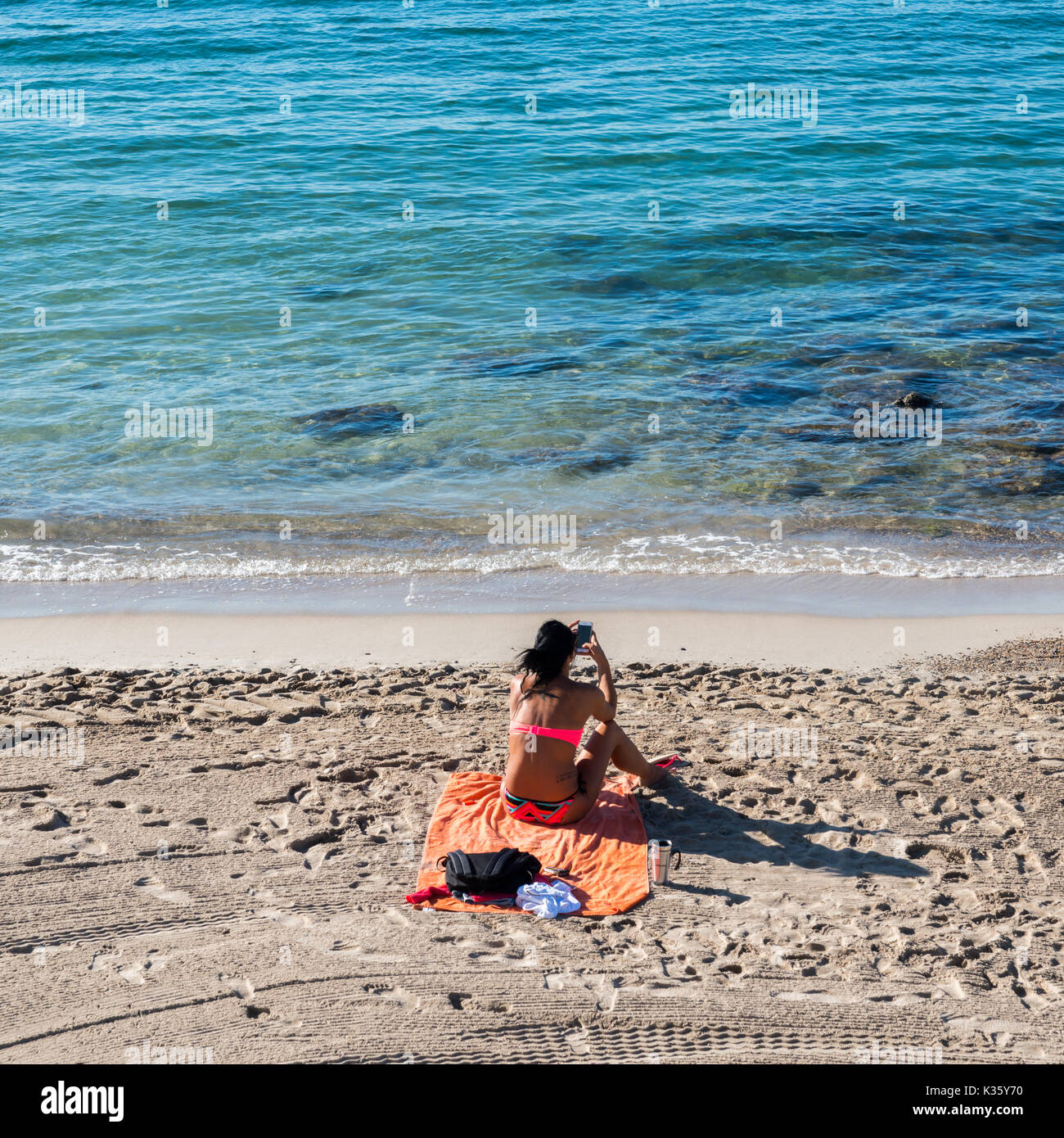 A woman on her smartphone on a beach in Nice, Cote d'Azur, France Stock Photo