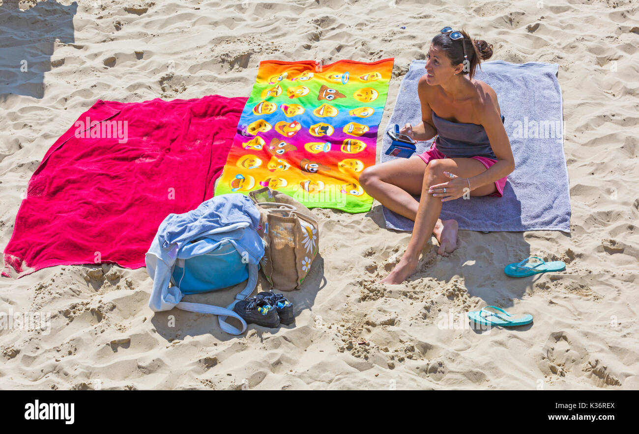 Bournemouth, Dorset, UK. 2nd Sep, 2017. UK weather: lovely warm sunny day at Bournemouth beach. Woman relaxing in the sun sitting on towel holding mobile phone iPhone smartphone cellphone. Credit: Carolyn Jenkins/Alamy Live News Stock Photo