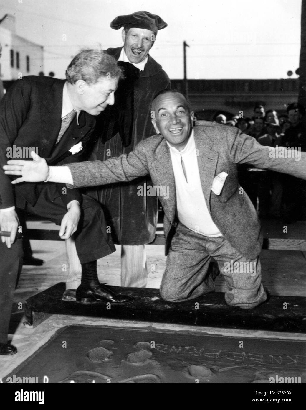Al Jolson celebrating just having made his hand, foot and knee-prints in the concrete at Sid Grauman's Chinese Theatre in hollywood. Sid Grauman is left looking directly at Jolson. Stock Photo