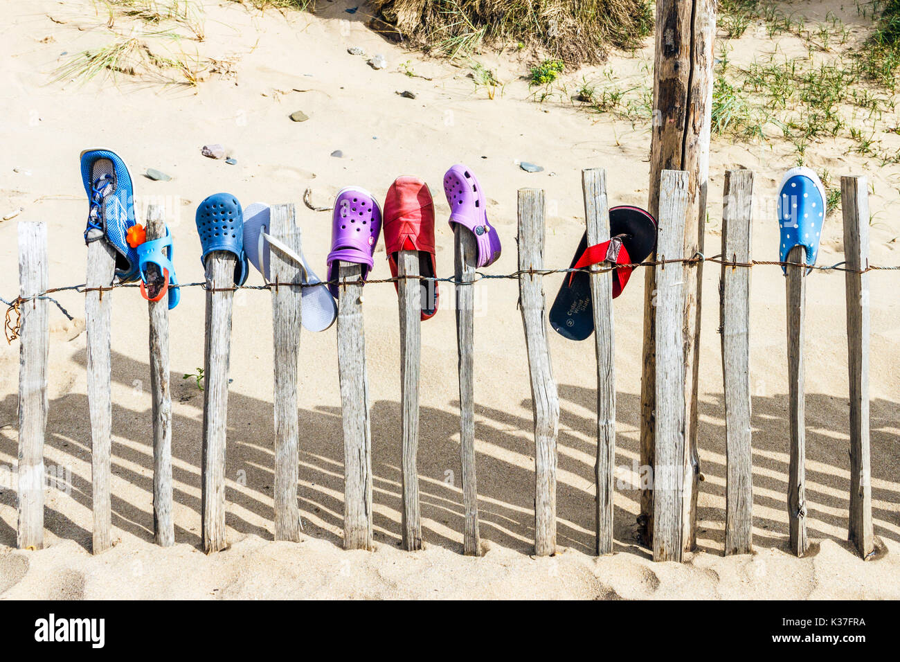 Lost shoes placed on a wooden paling fence on a sandy beach at Croyde, Devon, England, UK Stock Photo
