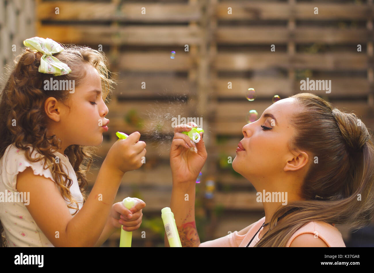 Happy little curly girl playing with soap bubbles on a summer nature with her mom, in a blurred background Stock Photo