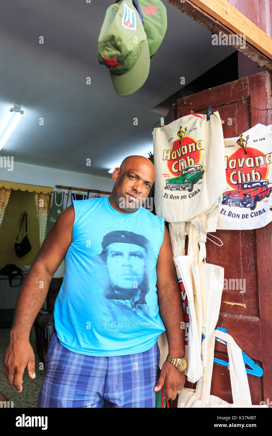 Cuban man in Che Guevara t-shirt selling tourist souveniers from typical makeshift living room shop, Habana Vieja, Cuba Stock Photo