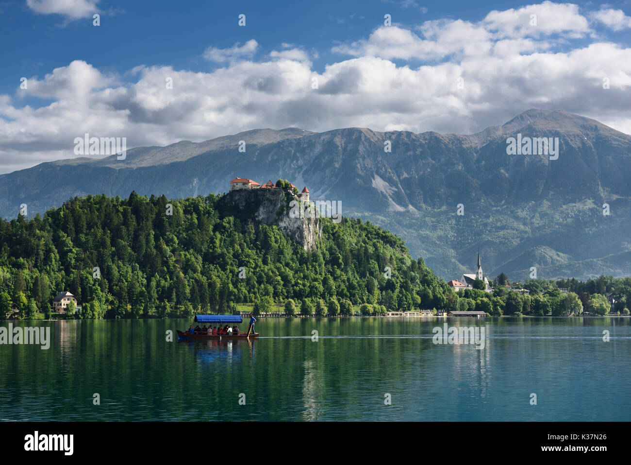 Traditional Pletna boat rowing tourists on Lake Bled with Bled castle ...