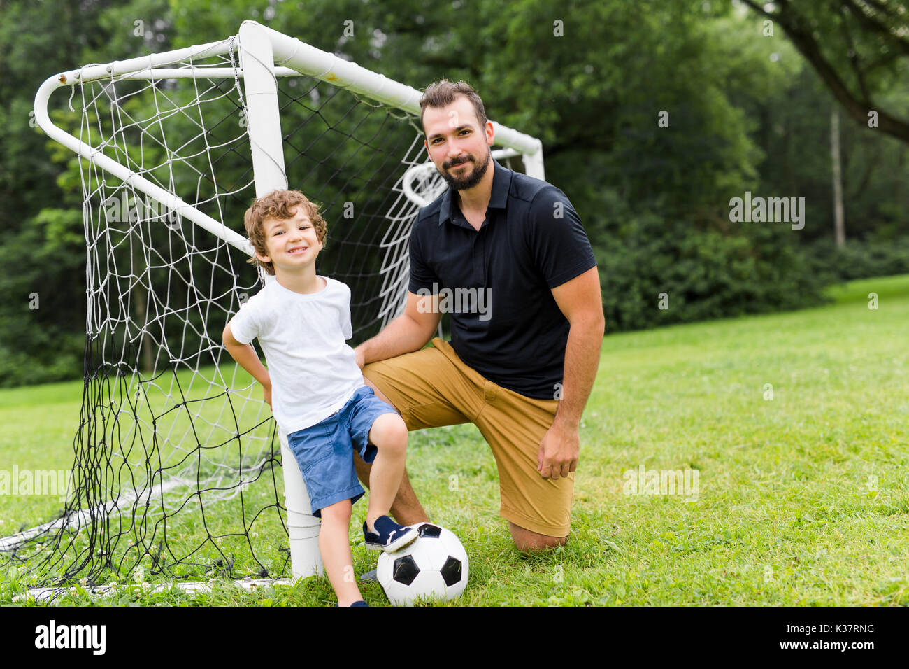 father with son playing football on football pitch Stock Photo