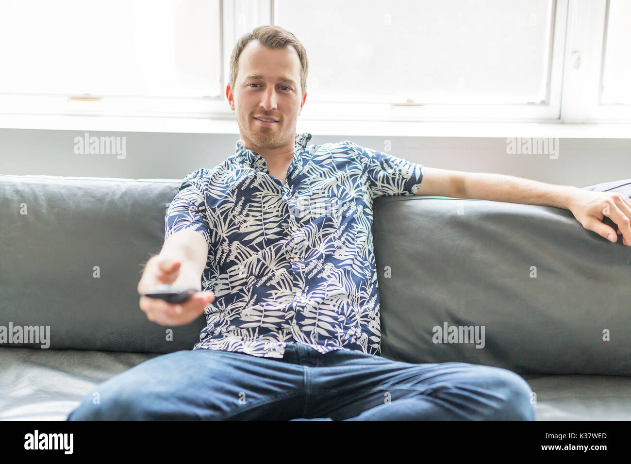 home, technology and entretainment concept - smiling man with tv remote control at home Stock Photo