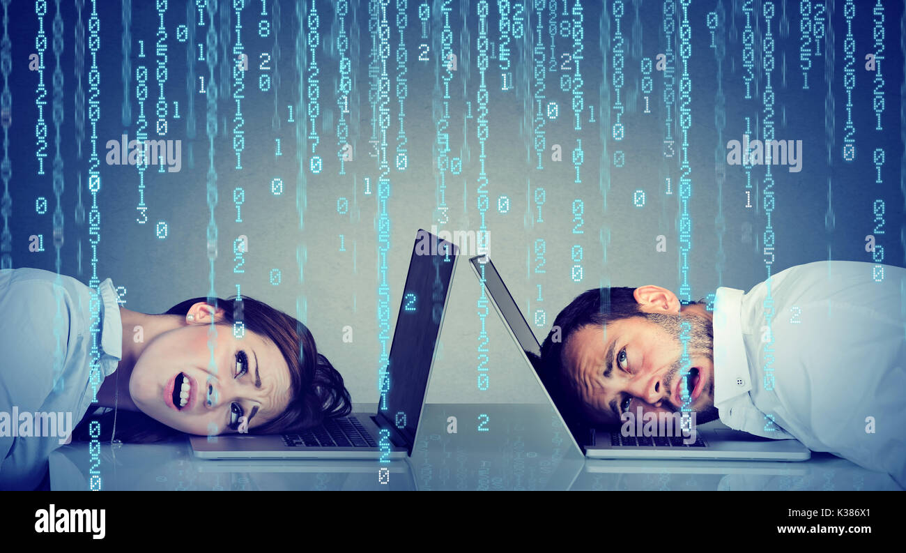 Stressed business woman and man resting head on laptop under binary code rain sitting at table frustrated with each other Stock Photo