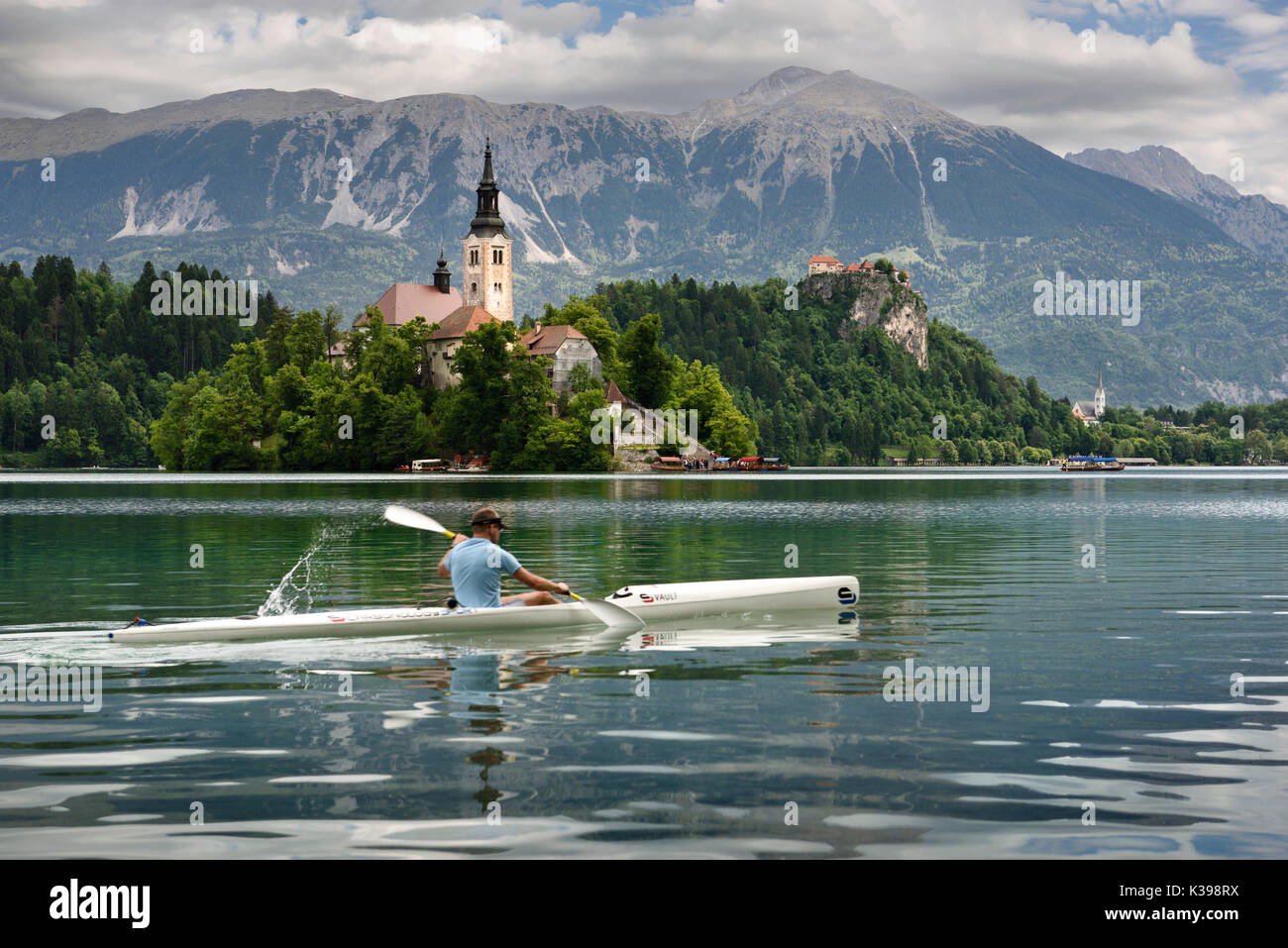 Assumption of Mary pilgrimage church Beld Island and kayaker on Lake Bled with Bled castle on cliff and Sol massive of Karavanke mountains Slovenia Stock Photo