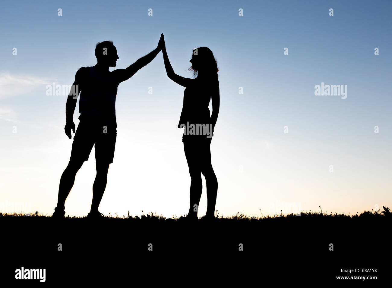 Happy silhouette couple holding up hands against the sky at dusk Stock Photo
