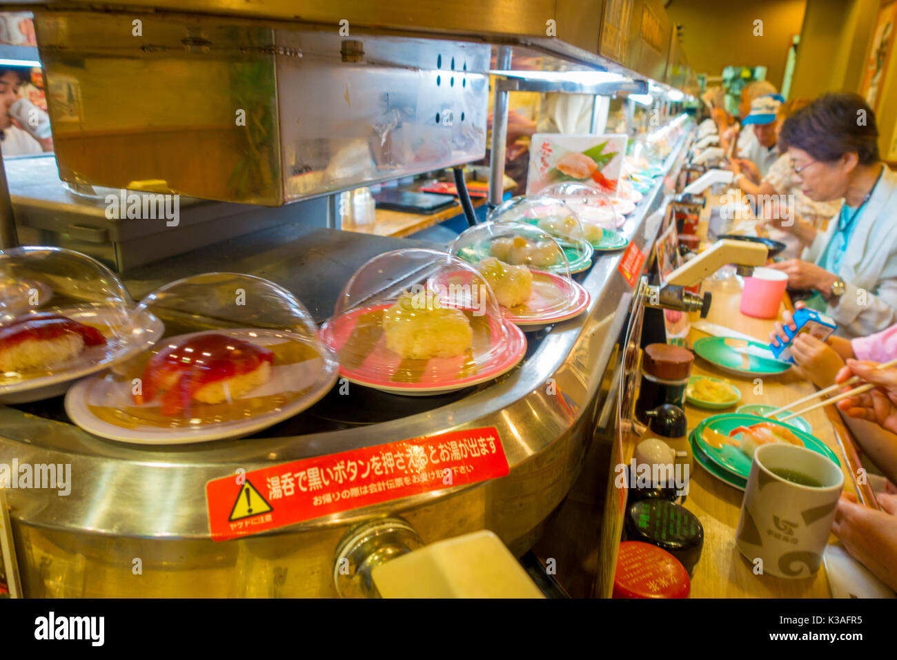 TOKYO, JAPAN -28 JUN 2017: Unidentified people eating an assorted japanesse food over a table, inside of a kaitenzushi conveyor belt sushi restaurant. Consumers pile up colored empty plates when they are finished eating, in Tokyo Stock Photo