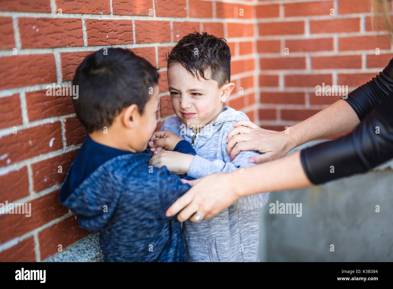 Teacher Stopping Two Boys Fighting In Playground Stock Photo