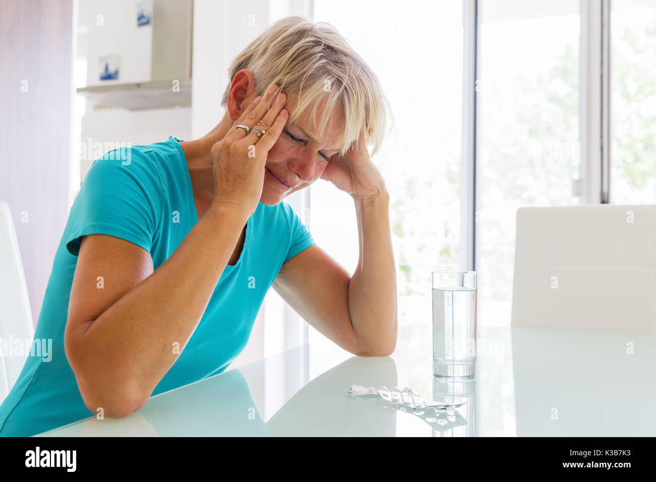 picture of a mature woman with headaches who sits in front of water and pills Stock Photo