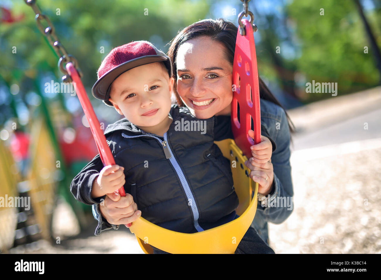 happy mother pushing son on swing in a park Stock Photo - Alamy