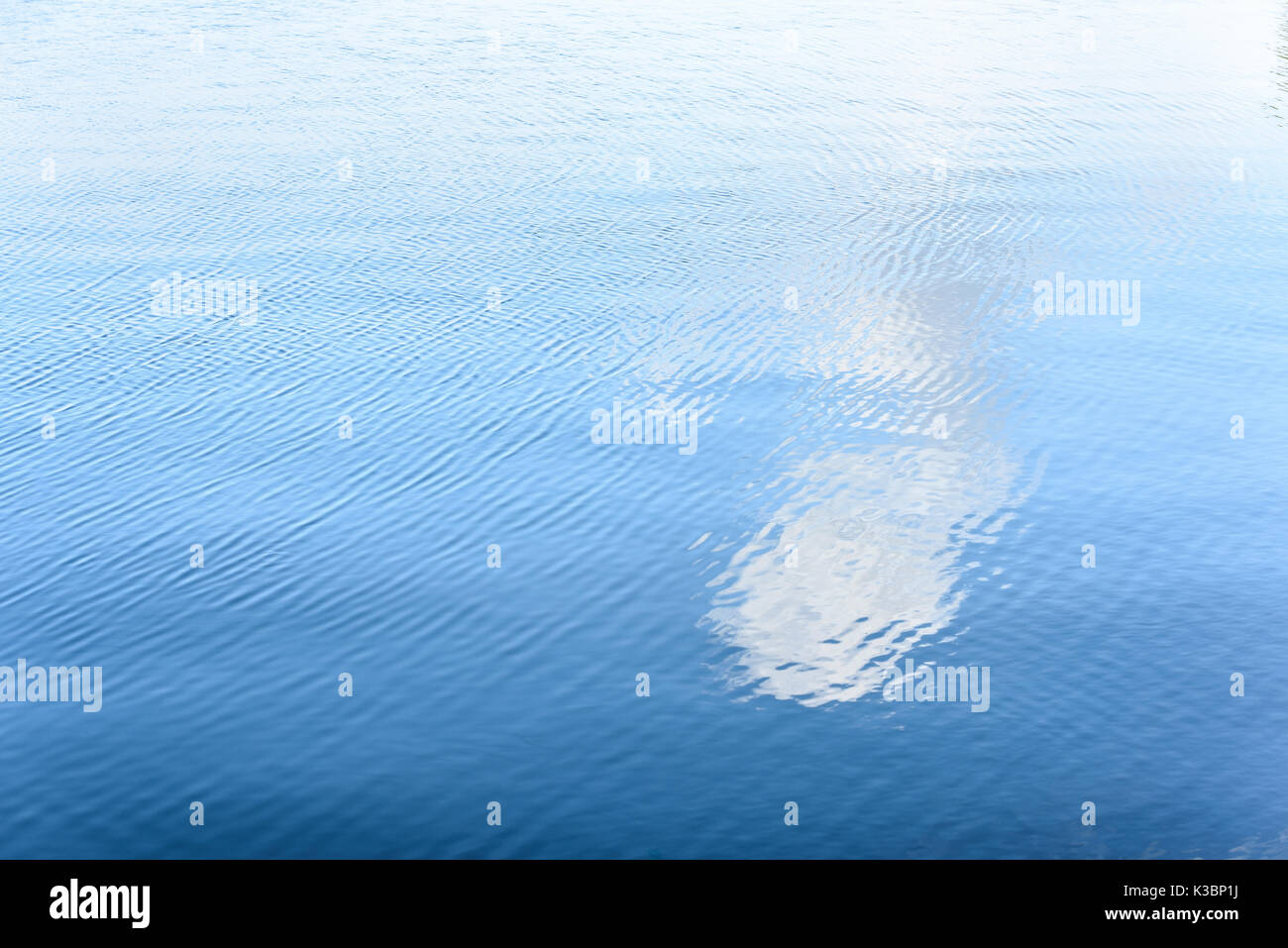 White cloud reflect in water surface with wave by gentle wind in summer time. Stock Photo