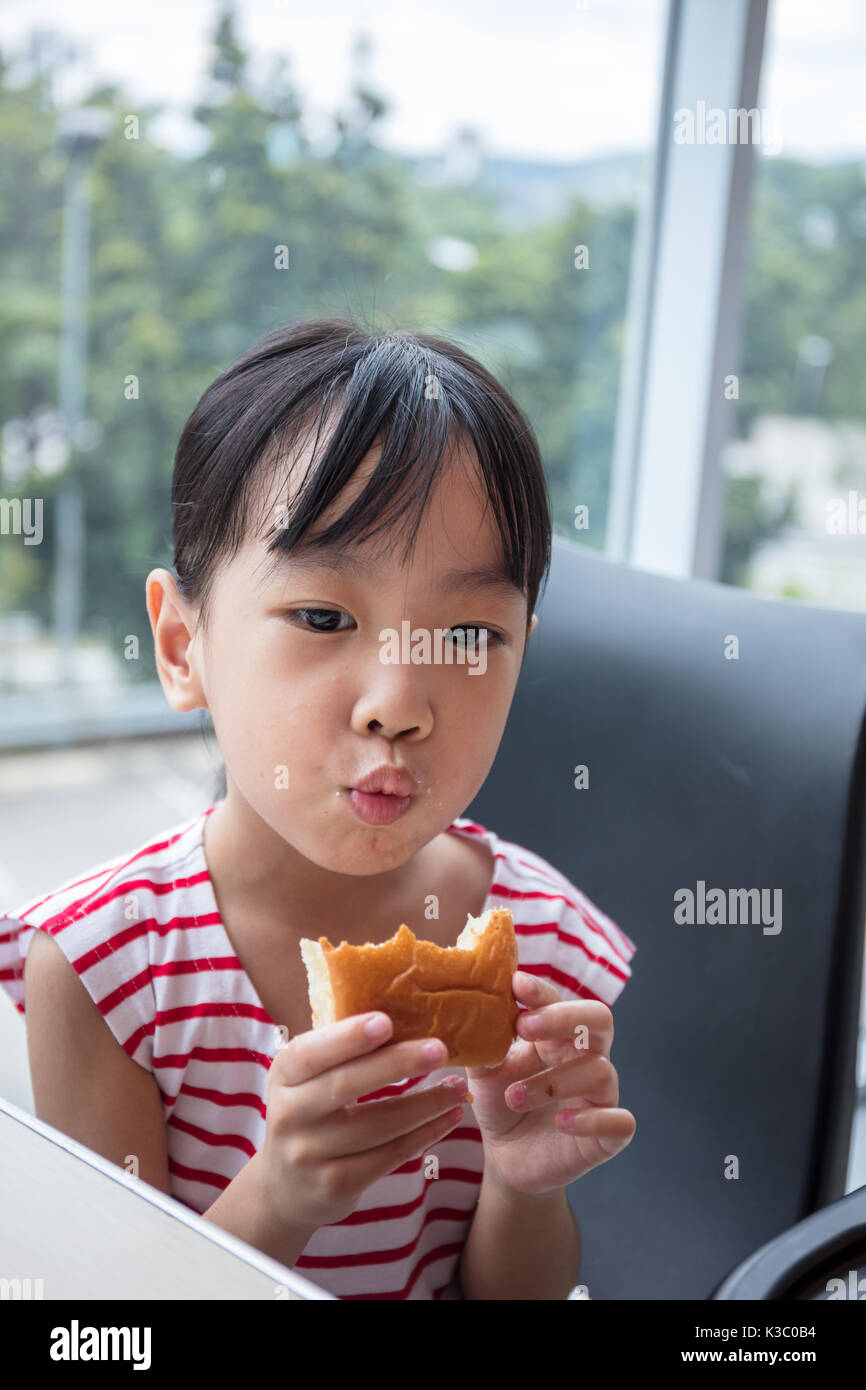 Asian Chinese little girl eating bread at indoor restaurant Stock Photo