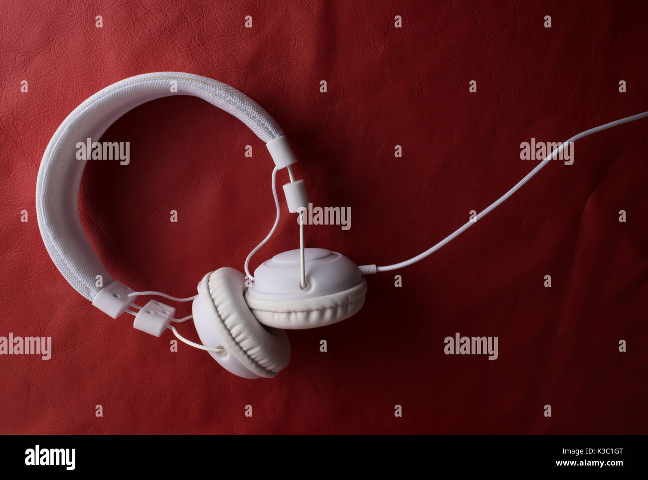 Isolated modern white headphone over a red leather background. Stock Photo