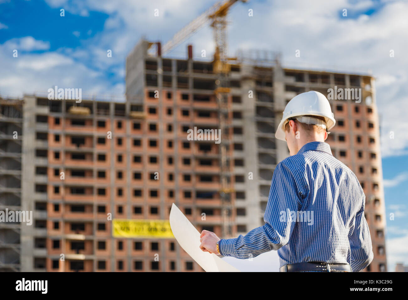 Architect in helmet with blueprints looks at camera in a building site Stock Photo