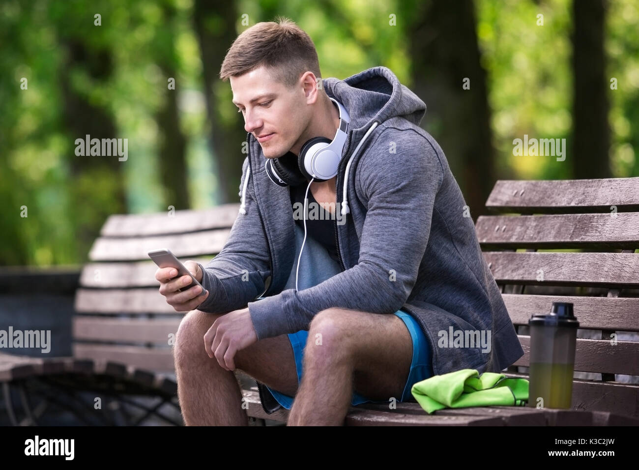 A photo of young man sitting on the bench and using mobile phone. He's resting after training. Stock Photo