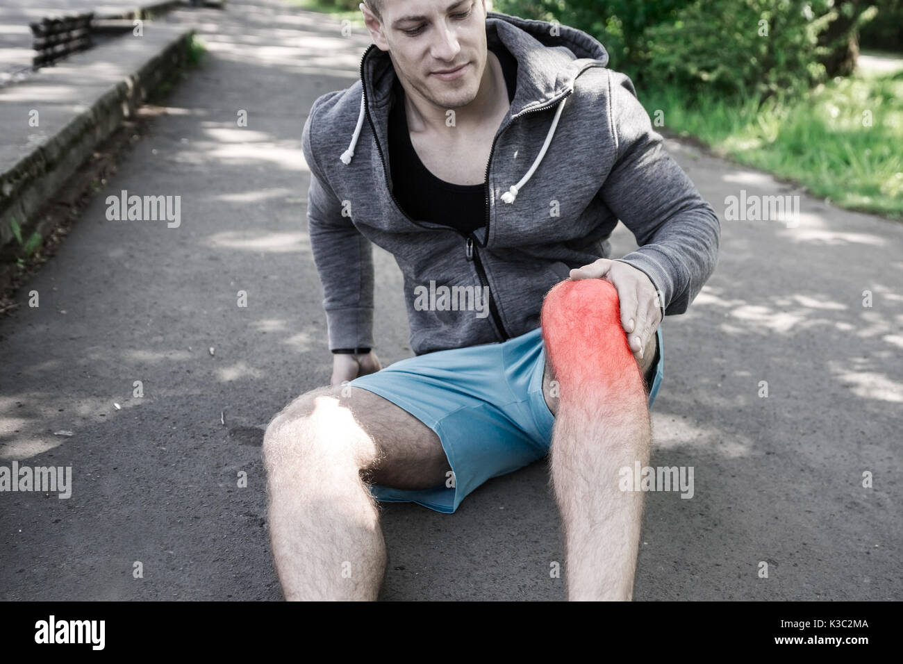 A photo of a man sitting down on the ground and suffering from knee injury. Stock Photo