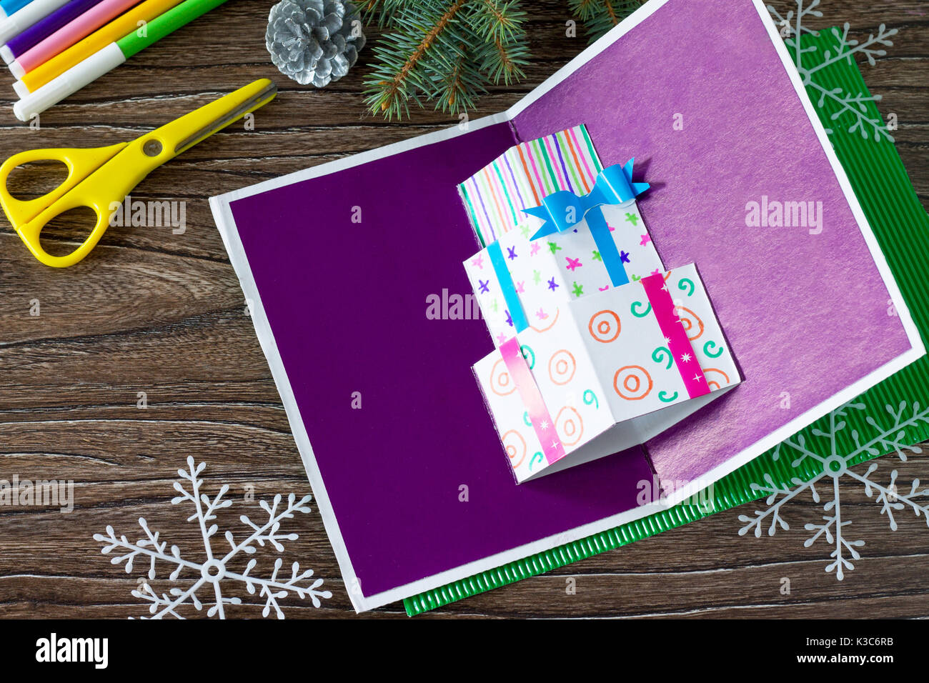 A child makes a birthday card with Christmas presents. Top view. Made by own hands. Children's art project, craft for children. Craft for kids. Stock Photo