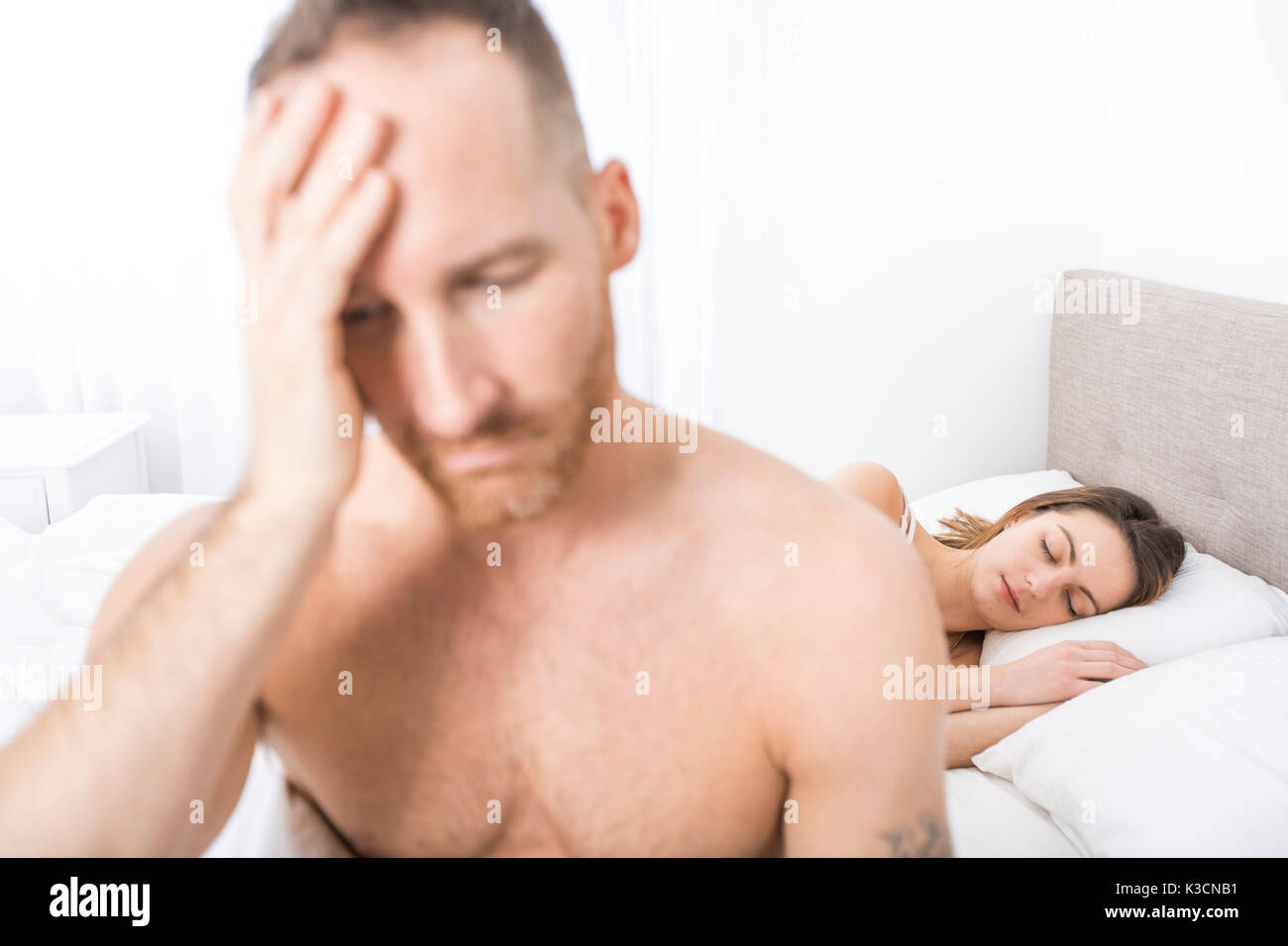 Depressed man sitting on the edge of the bed in bedroom Stock Photo