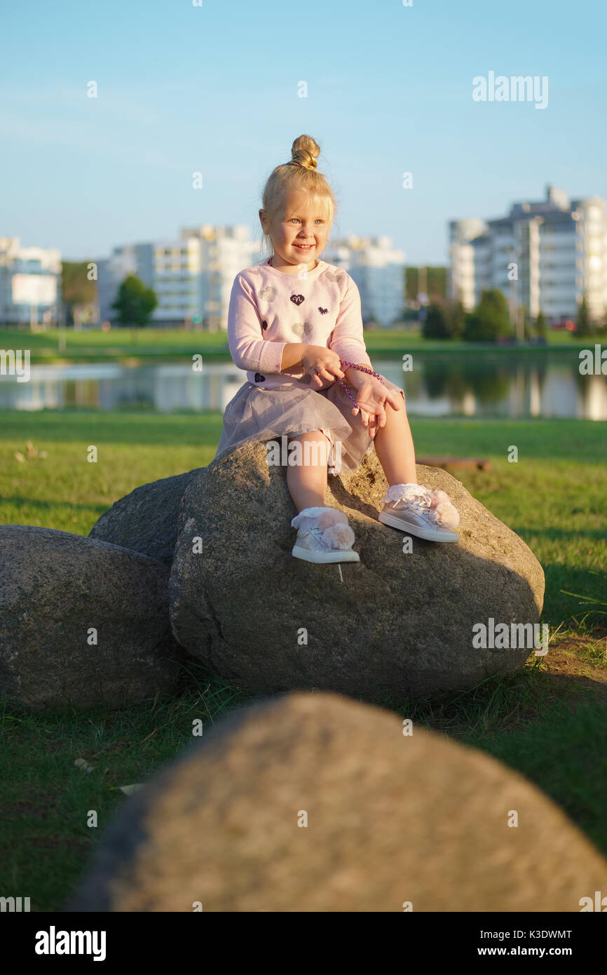 Little girl sitting on stone in sunset Stock Photo - Alamy