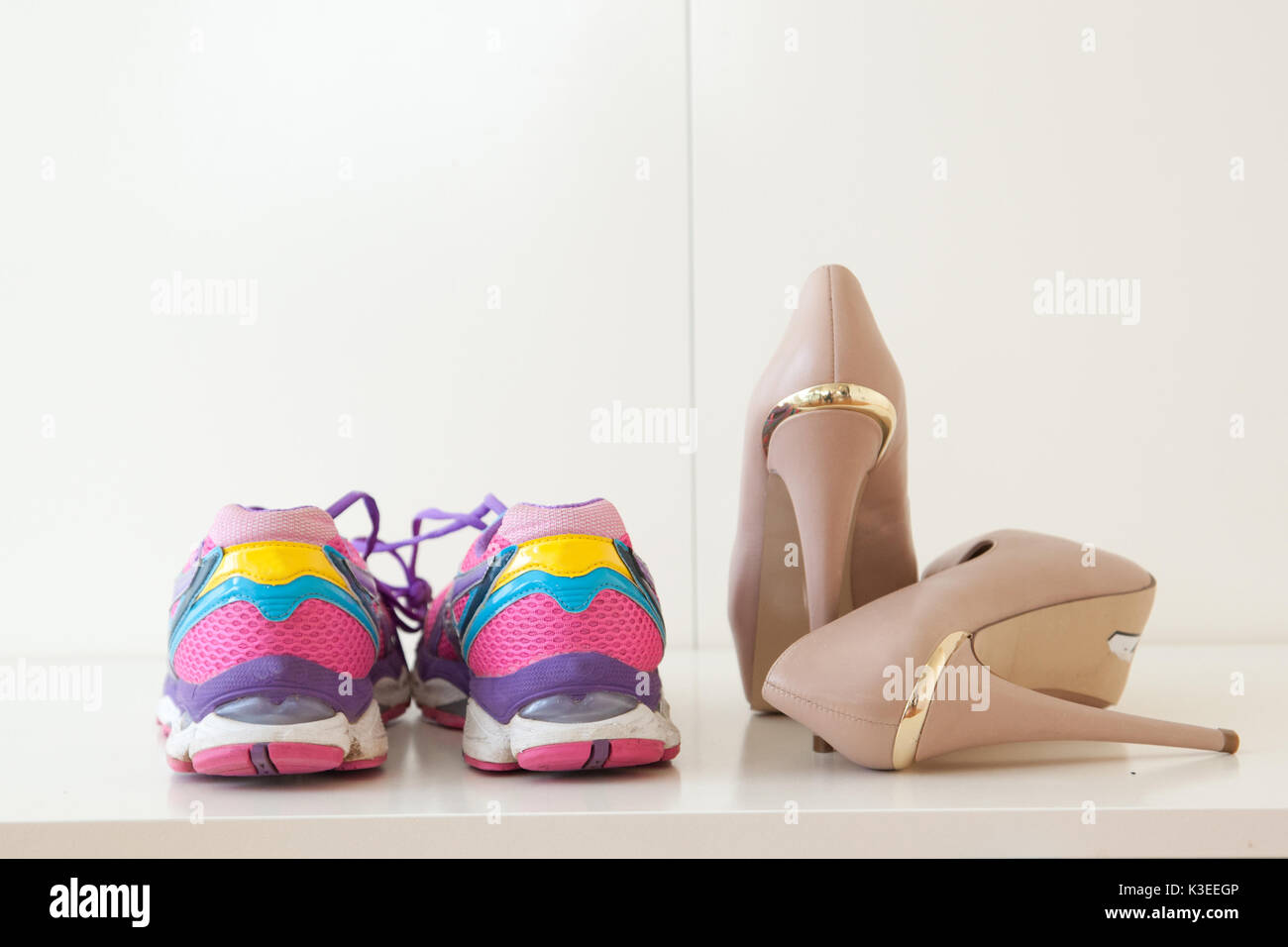 A pair of colorful sports shoes next to high heel stilettos. Stock Photo