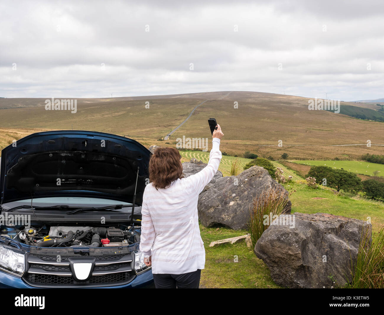 Mature, senior, attractive lady stranded in countryside with broken down care trying to get a cell phone signal to call for help. Stock Photo
