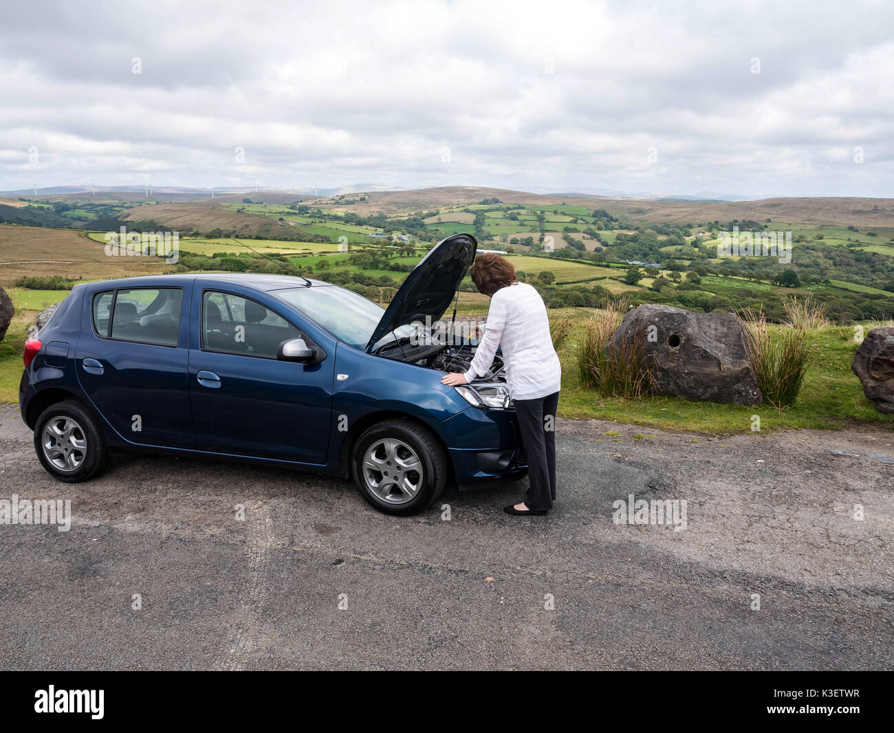 Mature attractive lady checking oil levels in the car engine looking at dipstick when stranded in the countryisde alone Stock Photo