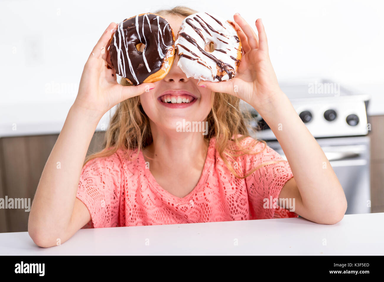 child playing with donuts in her hands putting them on her face Stock Photo
