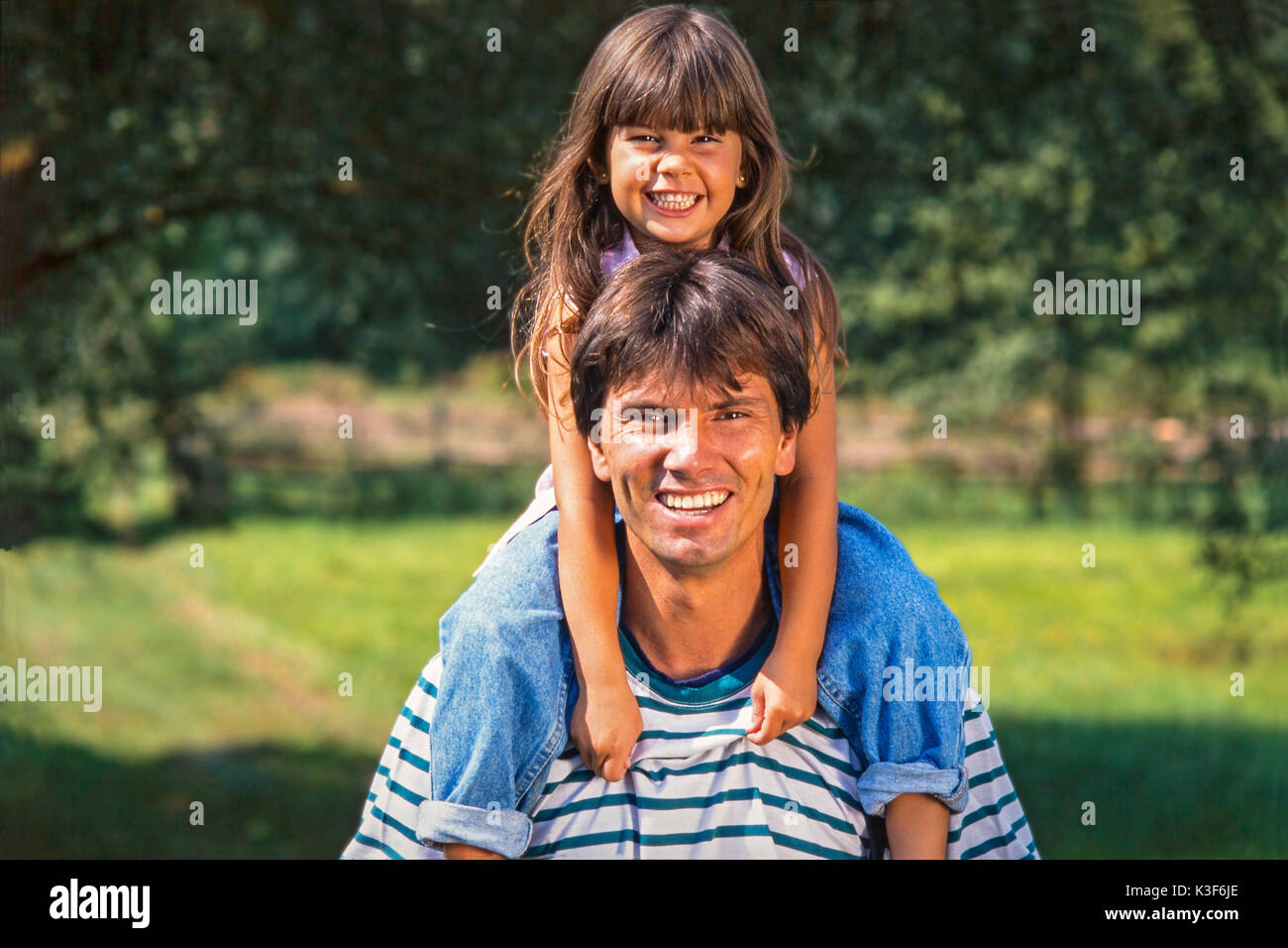 Father carries laughing daughter with brown long hairs on the shoulders Stock Photo