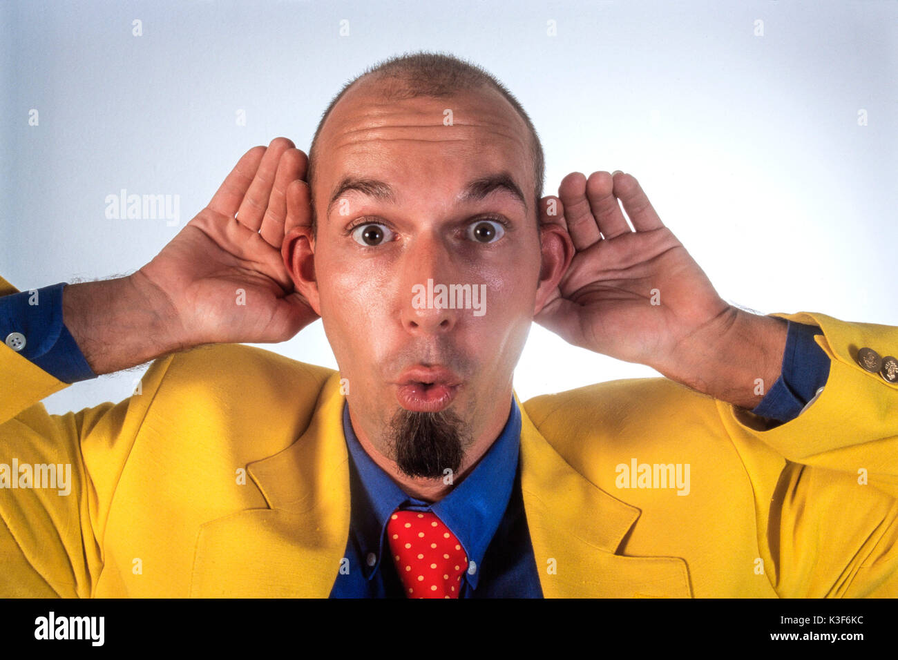 Man in a yellow sports jacket holds hands to the ears Stock Photo
