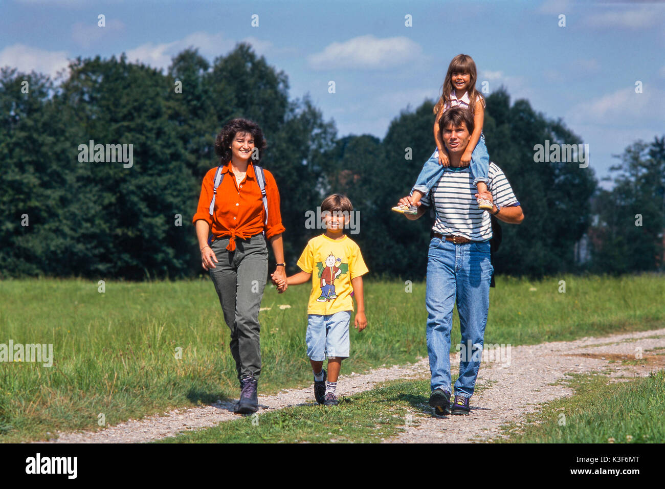 Family outing on foot, mother holds son in the hand, father carries daughter on the shoulders Stock Photo