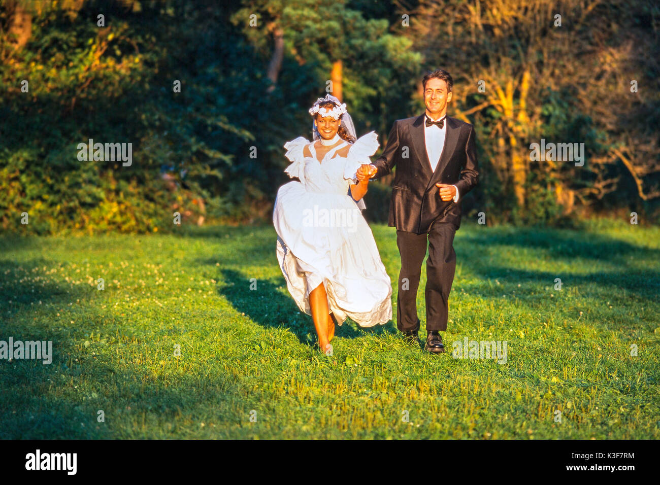 Bride and groom runs hand in hand over a meadow Stock Photo