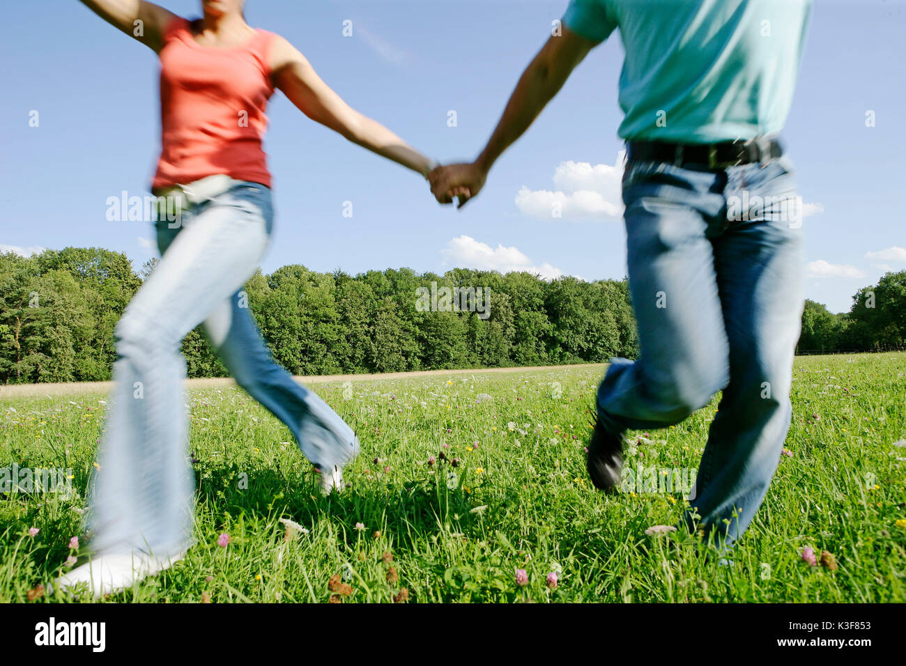 Young couple runs hand in hand over a meadow Stock Photo