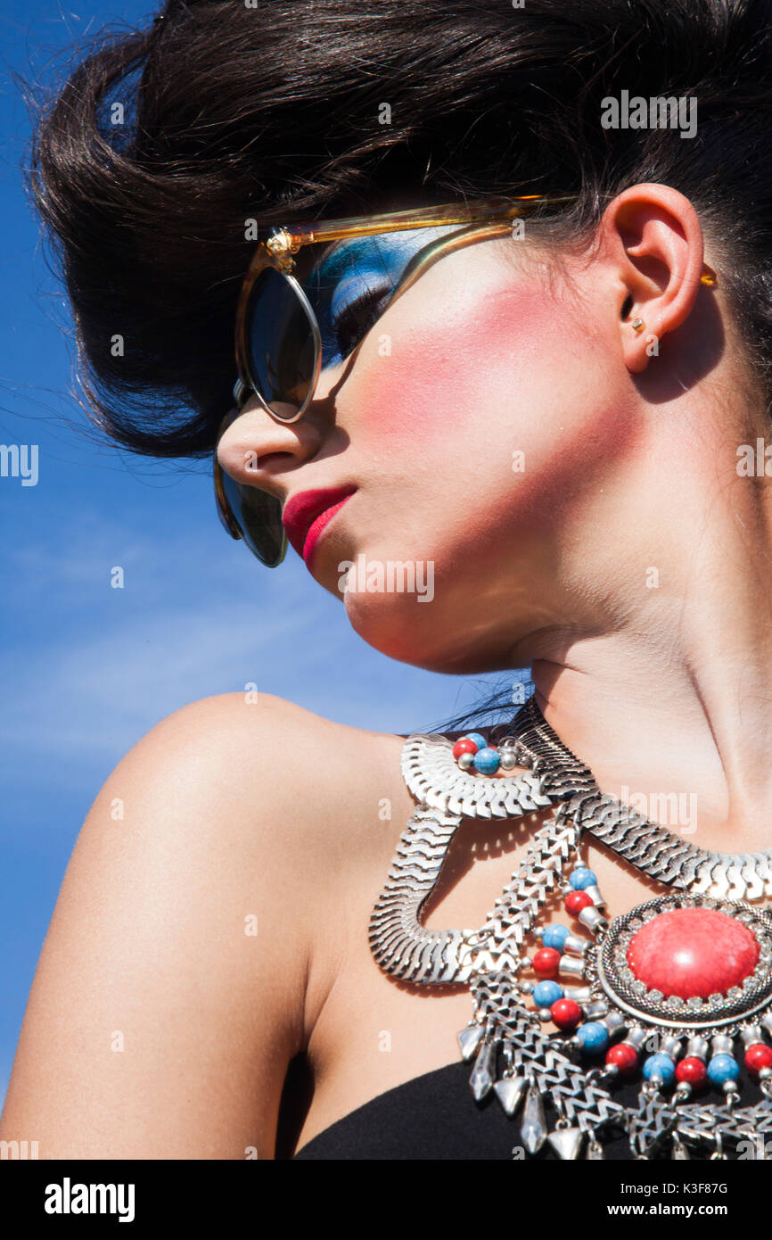 Profile Portrait of Young Adult Woman with Heavy Makeup Wearing Sunglasses and Large Necklace Stock Photo