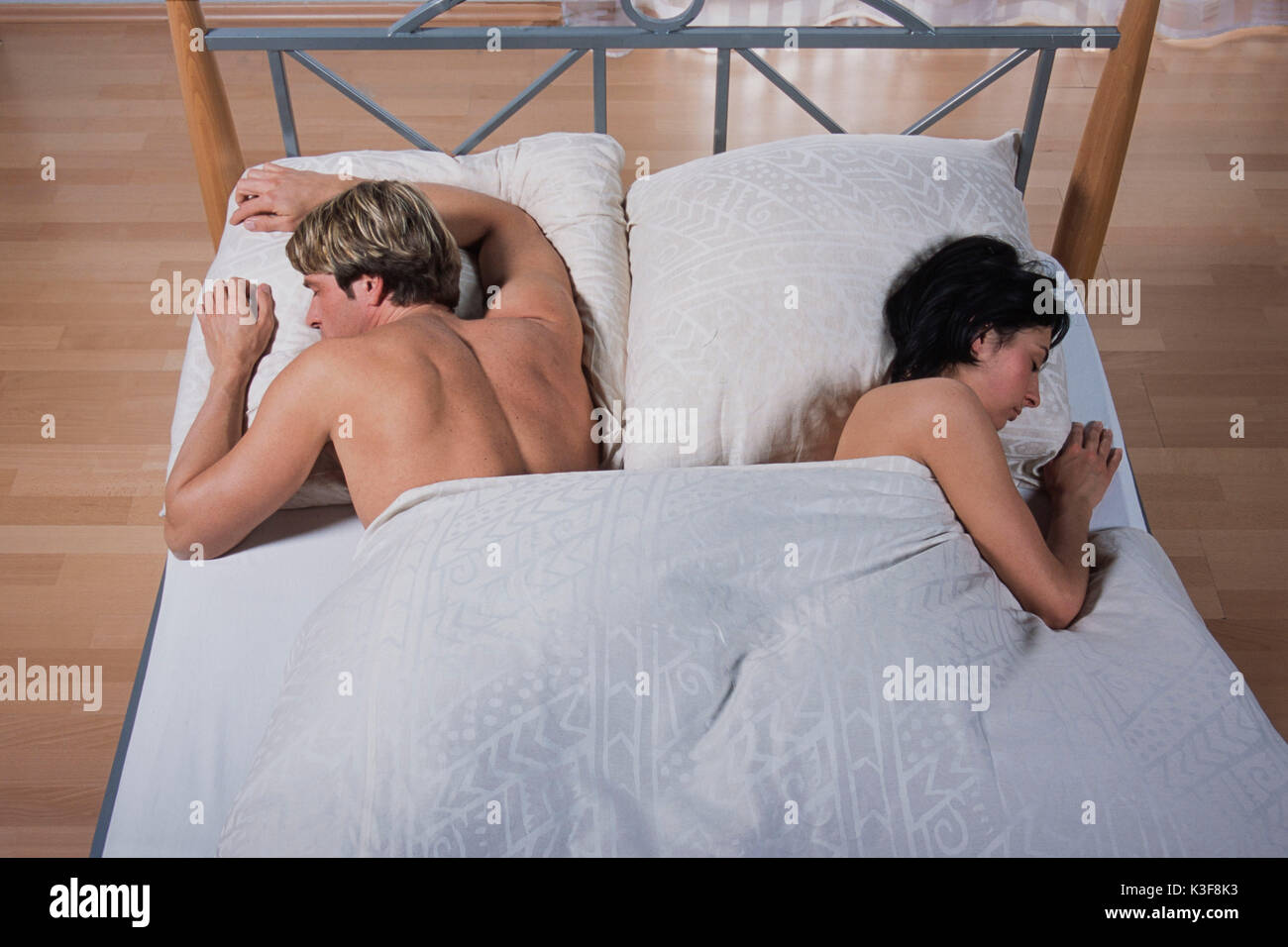 Young couple lies asleep in the bed, each other the backs turned off Stock Photo