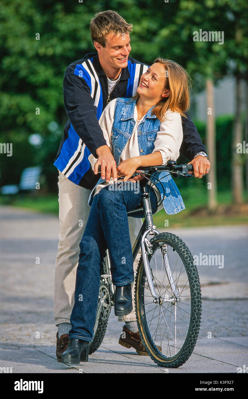 Young couple sits together on a mountain bike and look themselves at the  eyes Stock Photo - Alamy