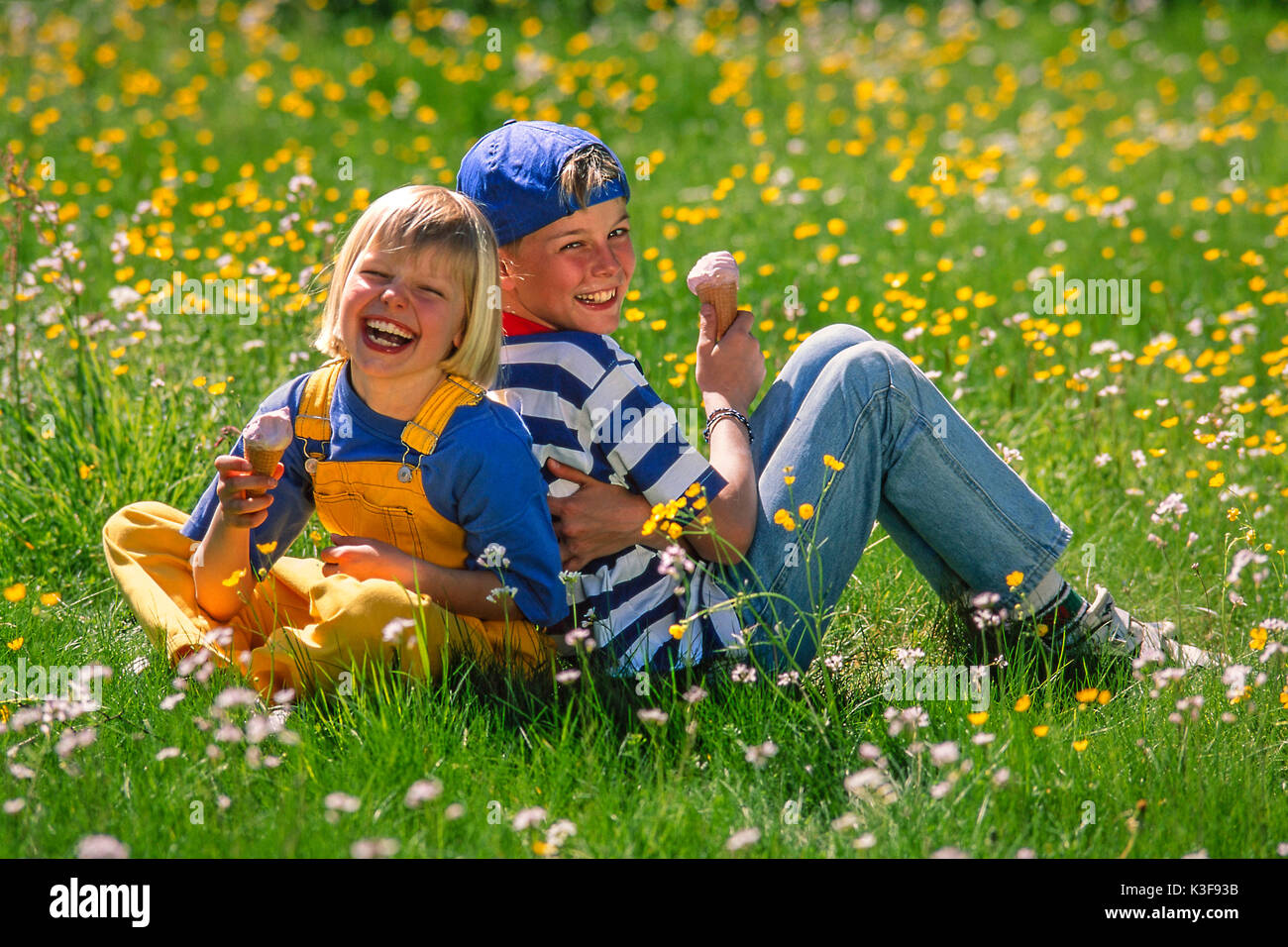 Two children sit in a spring meadow and eat ice Stock Photo