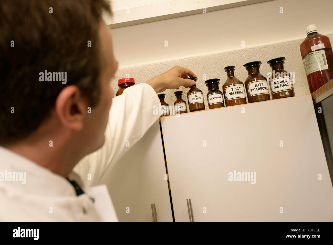 Chemist reaches for bottle on a cupboard Stock Photo